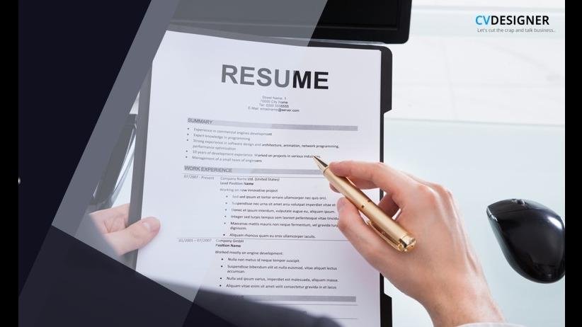 Person reviewing a printed resume with a pen in hand, next to a computer monitor.